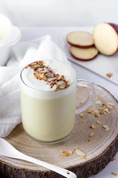 there is a cup of milk with nuts in it on the wooden plate next to some apples