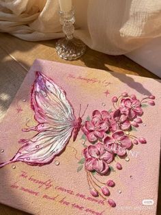 a card with pink flowers and a butterfly on it, sitting on a table next to a candle