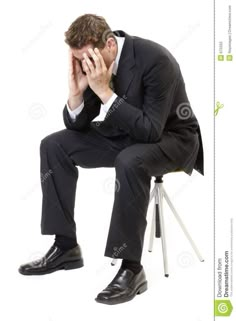 a man in a suit sitting on a chair and covering his face with his hands