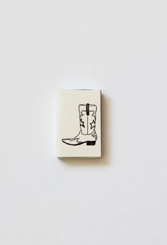 Say hi to our Western Cowgirl Matchbox! With a cute cowgirl boot and horseshoe illustration, this matchbox makes a trendy and unique gift. The ivory paper and black ink add a touch of sophistication, making it perfect for any occasion. Yeehaw! Size: 2.22" w x 1.375" h x .46" d Made in United States Cowboy Boot Matches, Retro Cowgirl Tattoo, Cowboy Boot Stamp Tattoo, Cowboy Match Holder, Vintage Cowgirl Tattoo Flash, Horseshoe Illustration, Cute Cowgirl, Forever Tattoo, Cute Cowgirl Boots