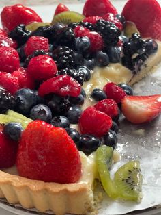 a pie with berries, kiwis and other fruits on the top is ready to be eaten