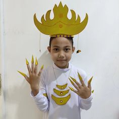 a young boy wearing a paper crown and holding his hands up to the camera while standing in front of a white wall