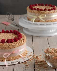 two cakes with fresh raspberries on top sit on plates next to a bowl of oatmeal