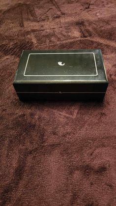 an empty black box sitting on top of a brown bed cover covered in red carpet