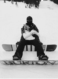 a man sitting on top of a snowboard next to another person in the snow