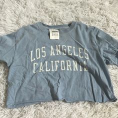 Brandy Melville Blue Los Angeles Cropped Tee. New With Tag. Light Wash Crew Neck T-shirt With Letter Print, Blue Letter Print Crew Neck Tops, Blue Crew Neck Top With Letter Print, Blue Cotton Graphic Print Crop Top, Blue Cotton Crop Top With Graphic Print, Blue Graphic Tee Cropped T-shirt With Relaxed Fit, Trendy Blue Tops For Loungewear, Trendy Blue Cotton Top, Blue Cotton Tops With Letter Print