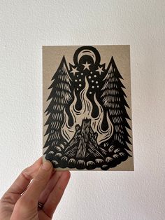 a hand holding up a piece of paper with an image of trees and mountains on it