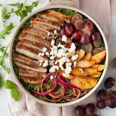 a bowl filled with meat, fruit and cheese on top of a table next to grapes