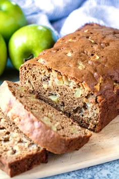 sliced loaf of bread sitting on top of a cutting board next to green apples