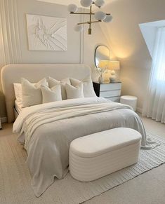 a white bedroom with a large bed, ottoman and mirror on the wall above it