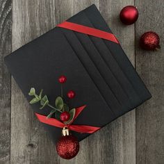 a black box with red ribbon and ornaments around it on a wooden floor next to christmas balls