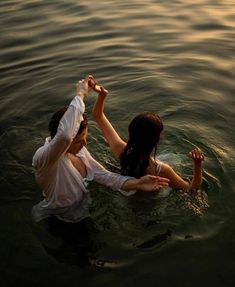 two people in the water holding hands and touching each other's foreheads,