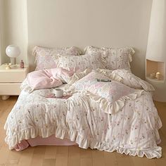 a bed with pink comforters and pillows in a room next to a white lamp