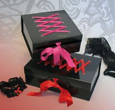 two black boxes with pink ribbons and bows on them, one is open to show the ribbon