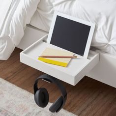 a laptop and headphones on a small table in front of a bed with white sheets