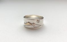 This beautiful band incorporates the majesty of the mountains and my love for the ocean all under a full moon 0.3ct diamond.  It is all hand fabricated using sterling silver for the base of the ring; it was also used to build the mountains and wave. The snowy mountain peak is highlighted by 10k yellow gold on the top of the middle mountain. The full moon diamond is perfectly set in a flush setting on a sterling silver raised base, to bring the full moon into view.  I hope this band captures your Silver Surf, Mountain Ring, Sea Glass Ring, Gold Waves, Wave Ring, Glass Rings, Timeless Wedding, Ring Diamond, Ring Collections