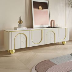 a white and gold sideboard with an art print on it's wall next to a potted plant