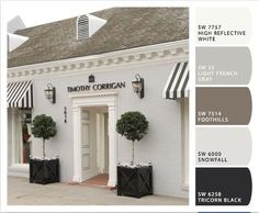 a white building with black and white awnings on the front, and two potted trees outside