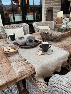 the table is set with coffee cups and plates on it, along with two wicker chairs