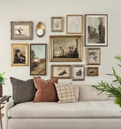 a living room filled with lots of framed pictures and paintings on the wall next to a couch