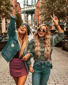 two women walking down the street with their arms in the air