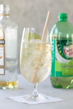 a glass filled with ice and lemonade next to two bottles of gin tonic water