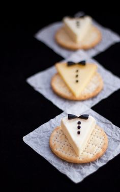 four crackers decorated with cheese and black bow ties are arranged in the shape of men's suits