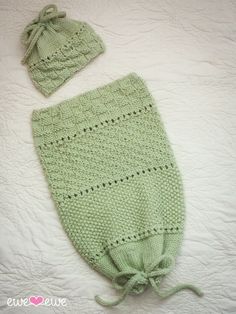 a green knitted hat and diaper cover laying on a white bed with the top knot undone