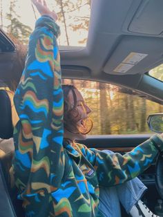 a woman sitting in the driver's seat of a car with her hand up