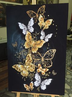 a painting with gold and white butterflies painted on it's black canvas, sitting on a easel