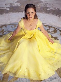 a woman in a yellow dress is sitting on the floor with her hands behind her back