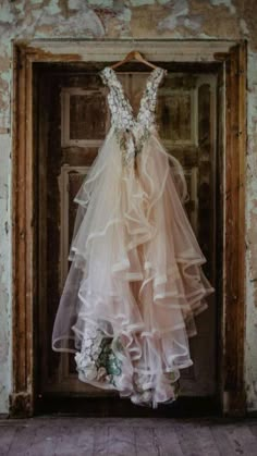 a wedding dress hanging on a door in an old building, with flowers all over it