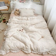 an unmade bed with a teddy bear on the pillow and some books in front of it