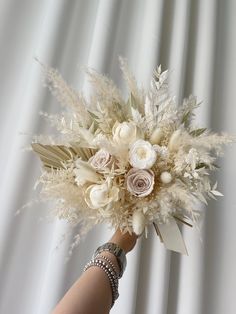 a woman's hand holding a bouquet of white flowers and pamyliums