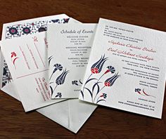 three wedding cards with blue and red designs on them sitting on top of a wooden table