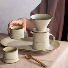 a person is holding three cups and saucers on a table with a spoon in front of them