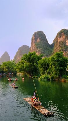 several people are rowing on small rafts in the water with mountains in the background