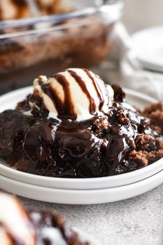 a white plate topped with chocolate dessert and ice cream on top of brownie crumbs