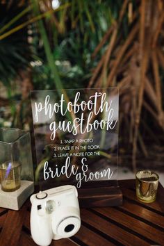 a wooden table topped with a sign next to a couple's wedding rings and binoculars