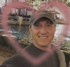 a man with a hat is smiling and posing for a photo in front of the water