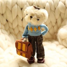 a small teddy bear holding a suitcase on a white surface with wool balls in the background