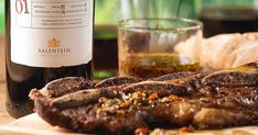 a bottle of wine sitting next to some steaks on a cutting board with bread