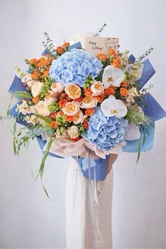 a woman holding a bouquet of blue and orange flowers in her hands with a note on it