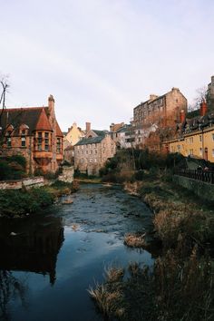 a river running through a lush green hillside next to tall brick buildings on either side