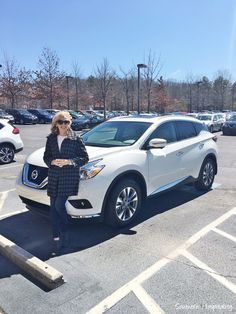 a woman standing next to a white car in a parking lot