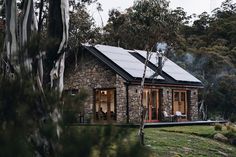 a small stone house with solar panels on the roof is surrounded by trees and grass