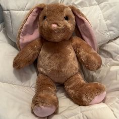 a brown stuffed animal sitting on top of a white comforter with pink ears and nose