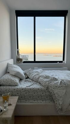 an unmade bed in front of a large window with the ocean out to sea