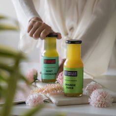 two bottles of orange juice sitting on top of a table next to flowers and plants