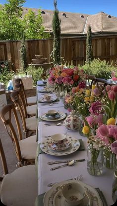 a long table with plates and flowers in vases on top of it next to a wooden fence